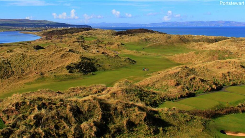 Coastal golf course landscape with rolling green hills, sandy dunes, and ocean view under a clear blue sky at Portstewart.